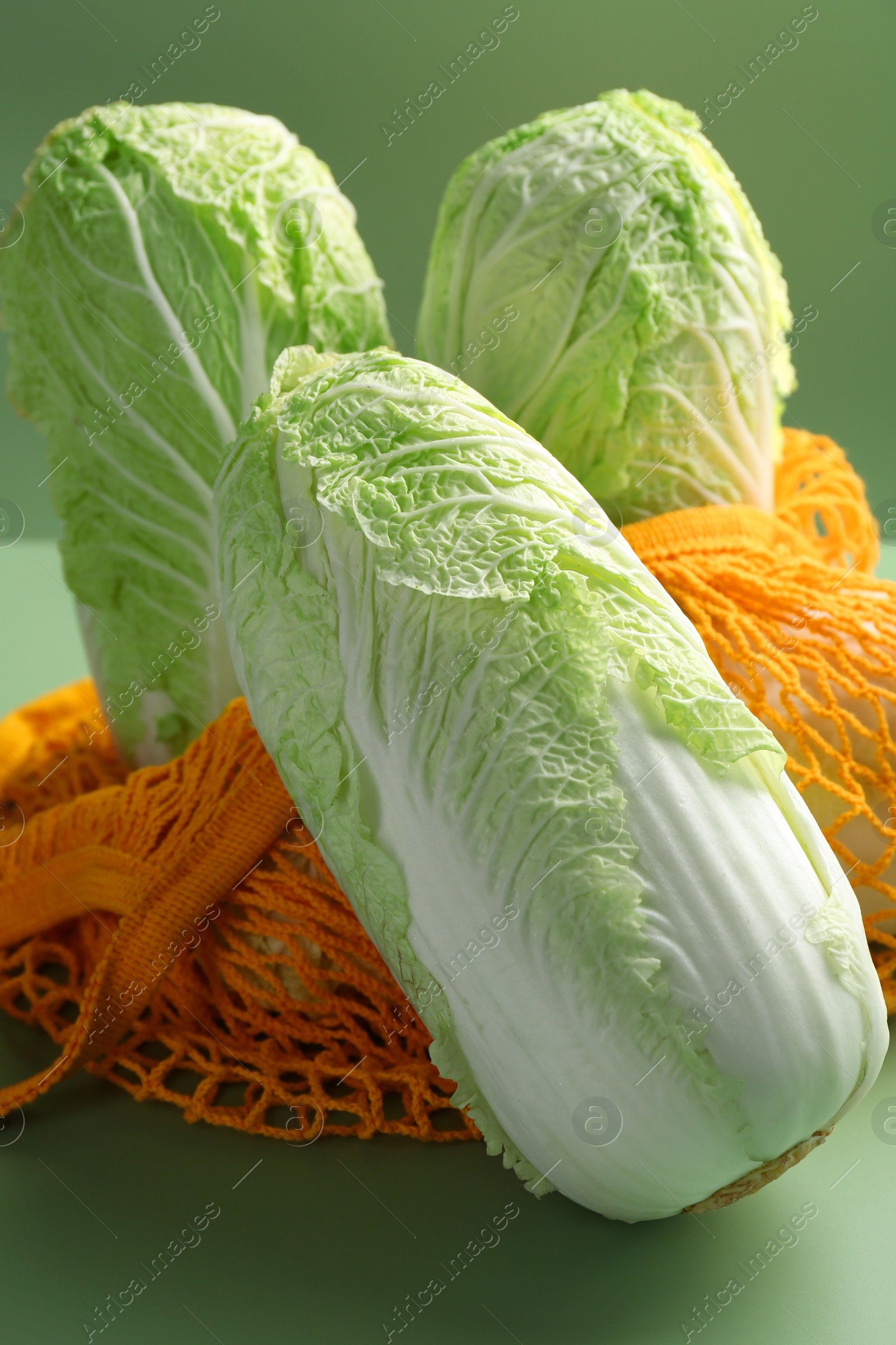 Photo of Fresh Chinese cabbages and string bag on green background, closeup