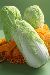 Photo of Fresh Chinese cabbages and string bag on green background, closeup