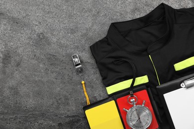 Referee jersey, whistle and other equipment on grey table, top view. Space for text