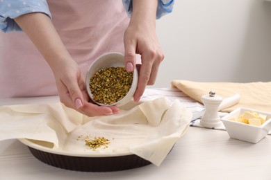 Photo of Woman putting filling into baking dish with dough to prepare baklava at white wooden table, closeup