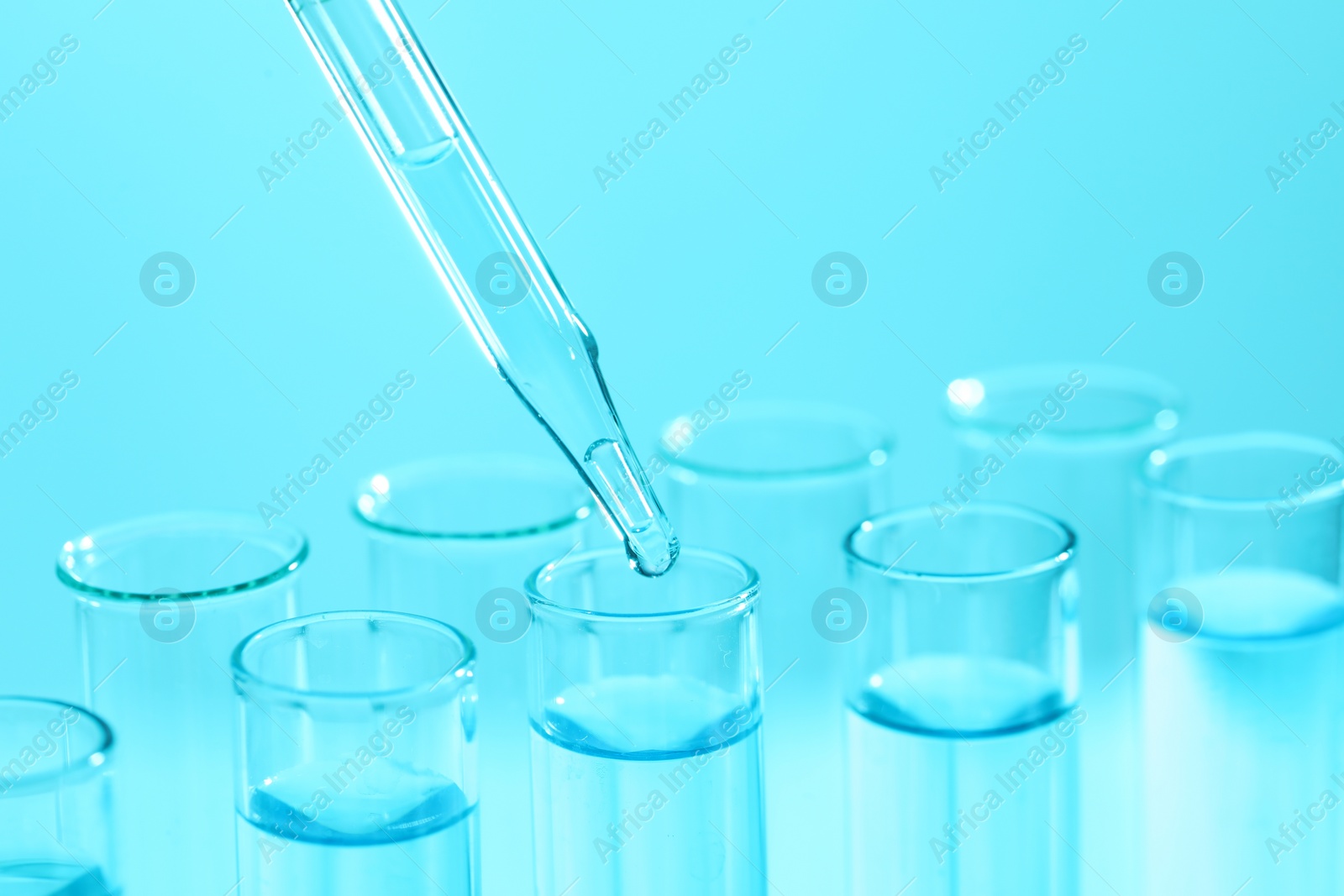 Photo of Dripping liquid from pipette into test tube on light blue background, closeup. Laboratory analysis