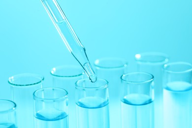 Photo of Dripping liquid from pipette into test tube on light blue background, closeup. Laboratory analysis