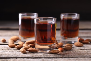 Photo of Shot glasses with tasty amaretto liqueur and almonds on wooden table, closeup