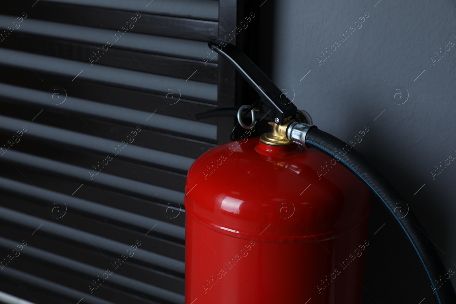 Photo of Fire extinguisher near grey wall indoors, closeup. Space for text