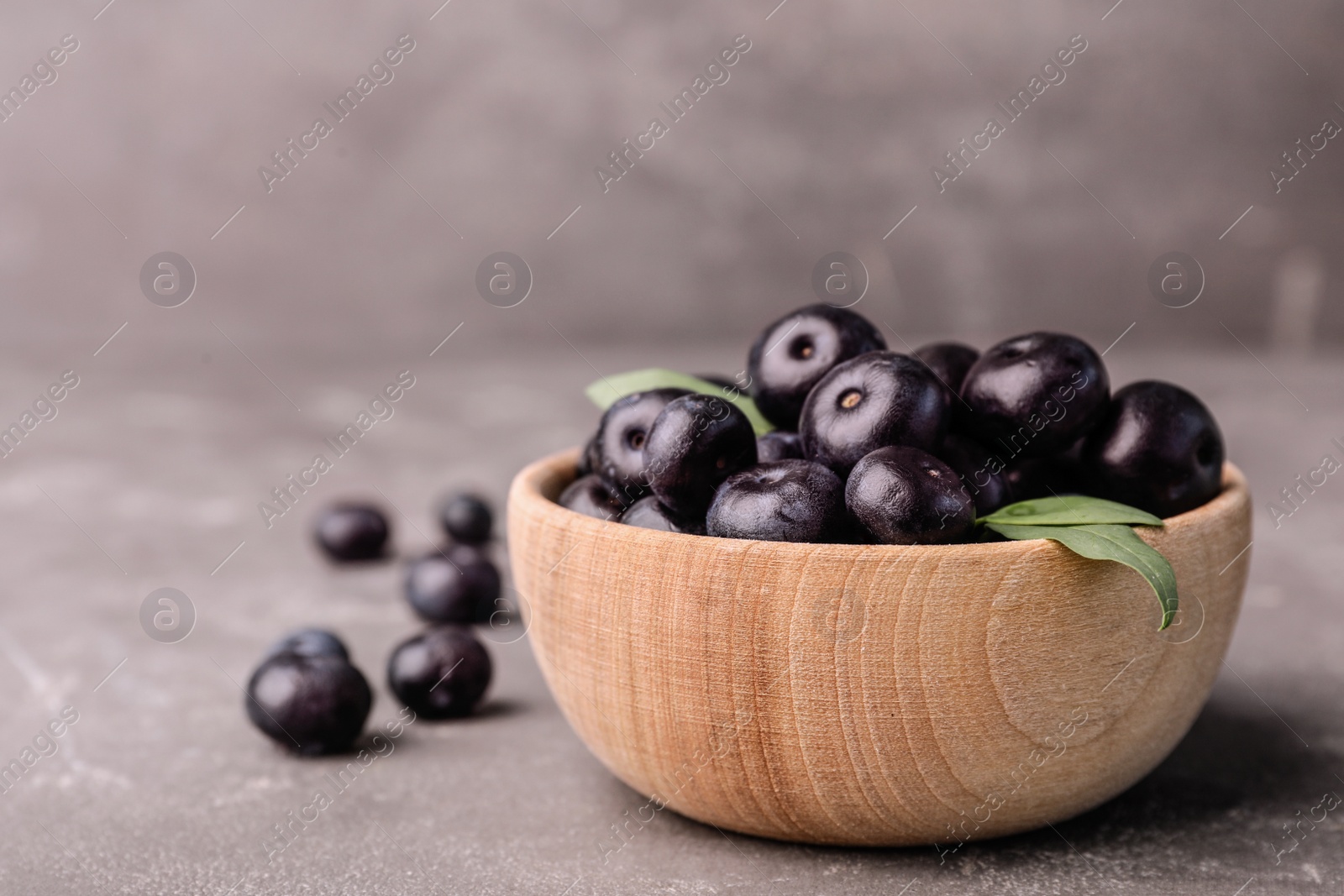 Photo of Bowl of fresh acai berries on grey stone table, closeup. Space for text