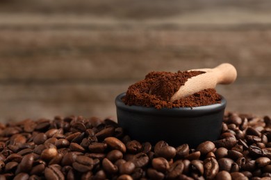 Bowl with scoop and ground coffee on roasted beans, closeup