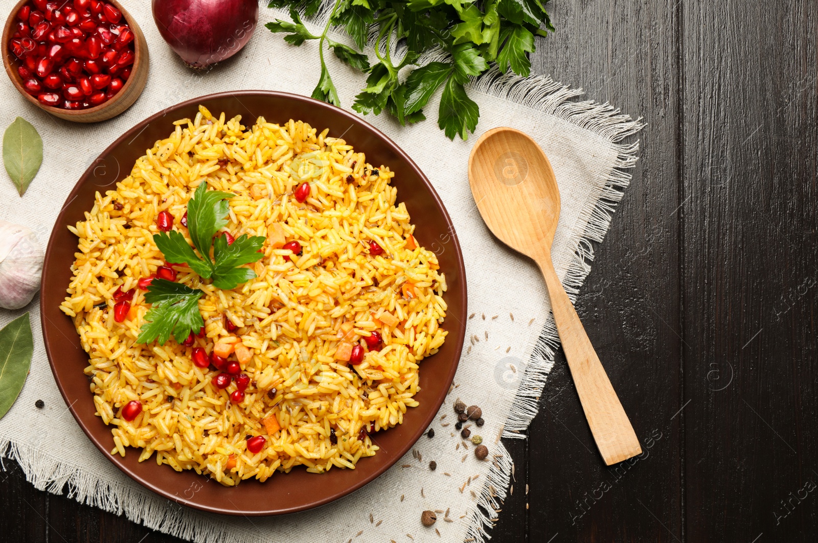 Photo of Tasty rice pilaf with pomegranate grains served on black wooden table, flat lay