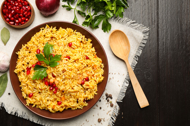 Photo of Tasty rice pilaf with pomegranate grains served on black wooden table, flat lay