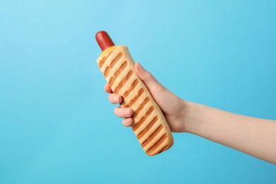 Photo of Woman holding delicious french hot dog on light blue background, closeup