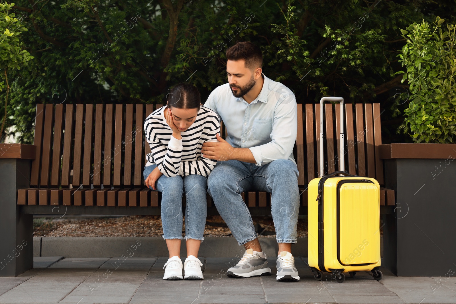 Photo of Long-distance relationship. Man calming his sad girlfriend on bench and suitcase outdoors