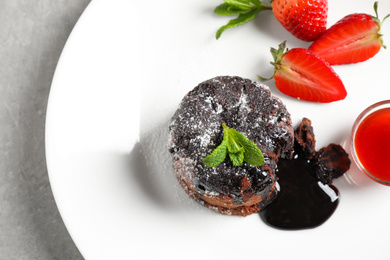 Photo of Delicious warm chocolate lava cake with mint and strawberries on plate, above view