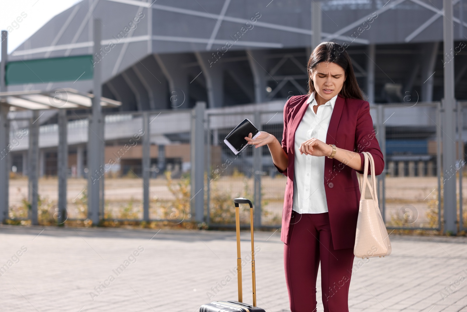 Photo of Being late. Worried businesswoman with suitcase and passport looking at her watch outdoors, space for text