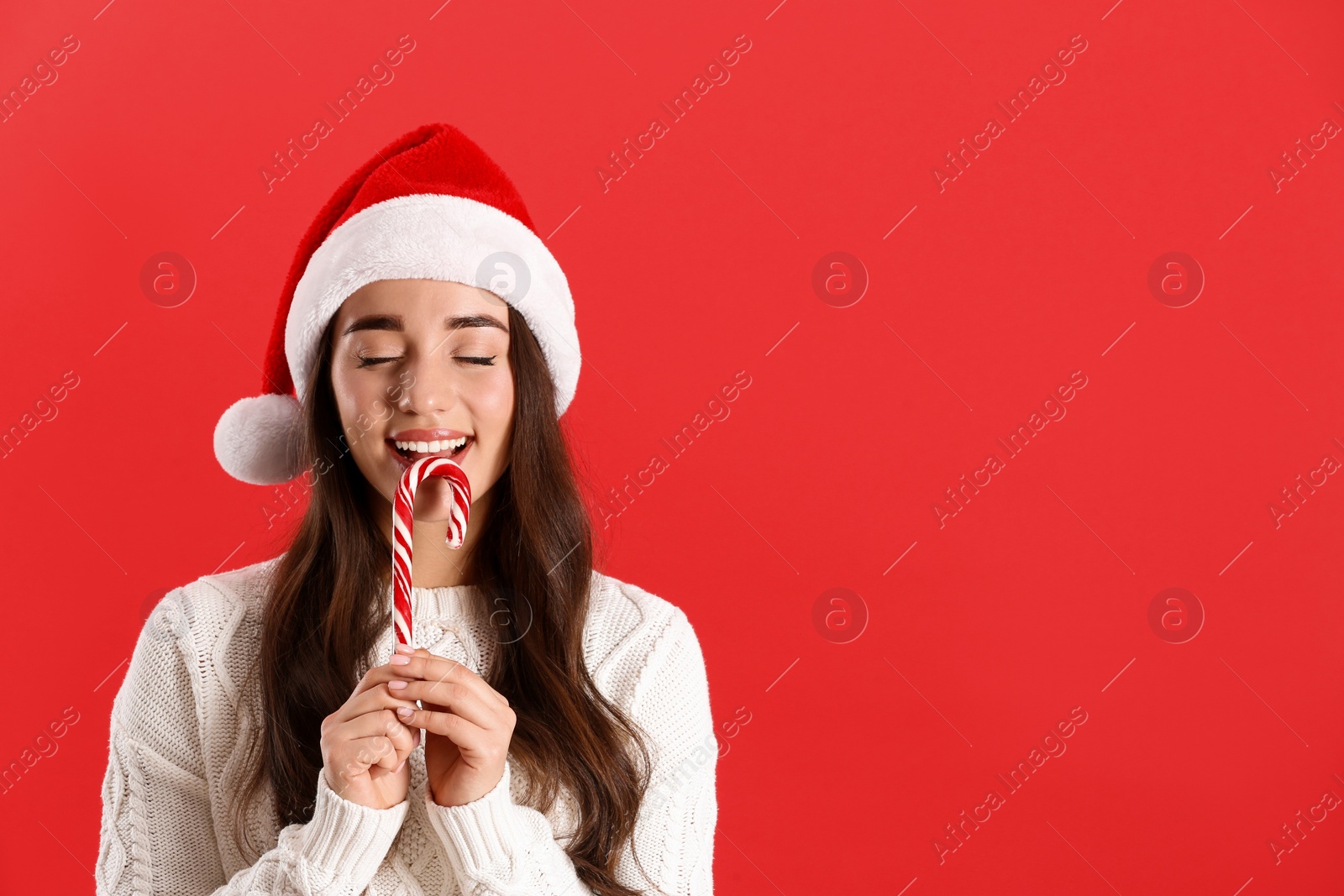 Photo of Beautiful woman in Santa Claus hat holding candy cane on red background. Space for text