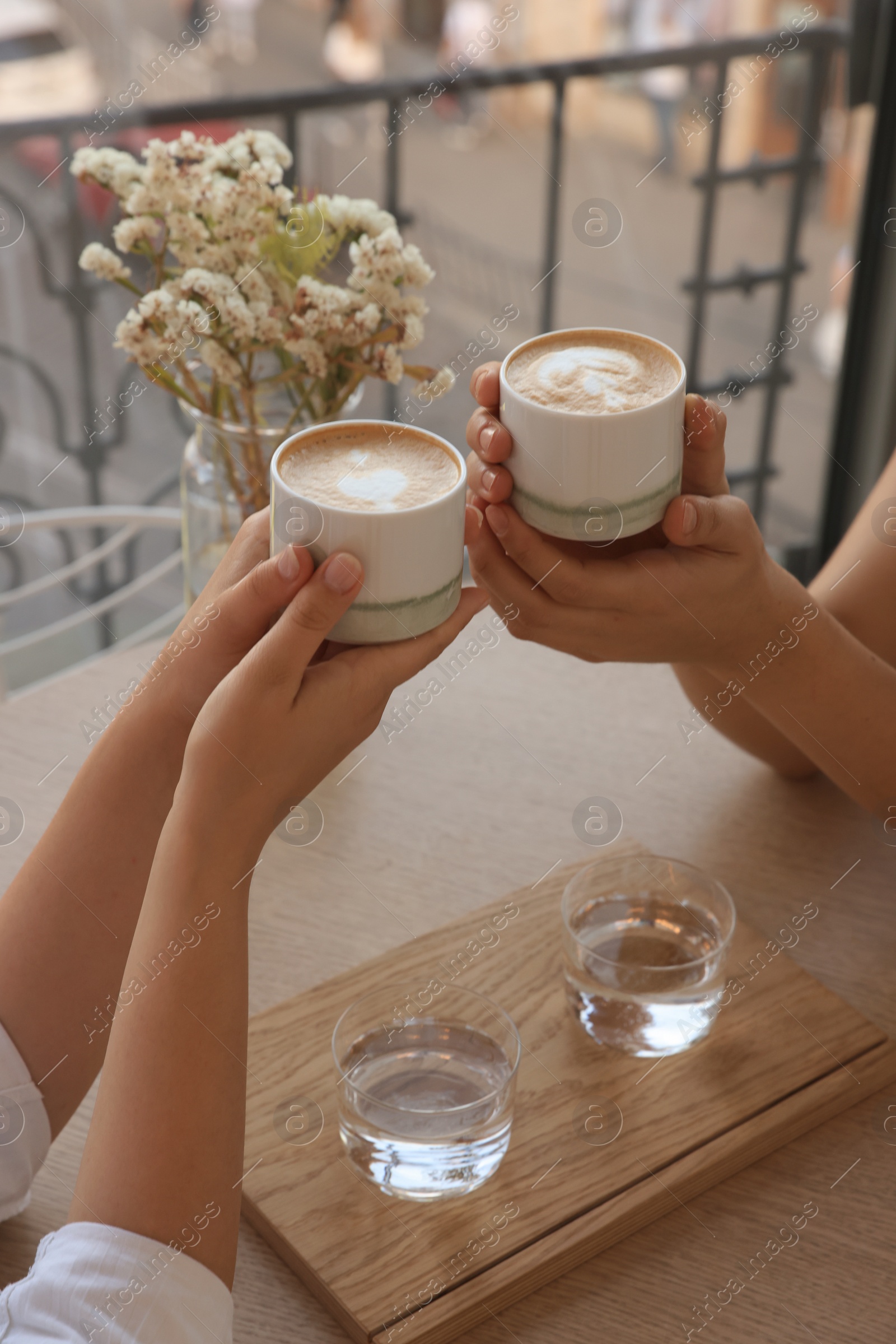 Photo of Friends drinking coffee at wooden table in cafe, closeup