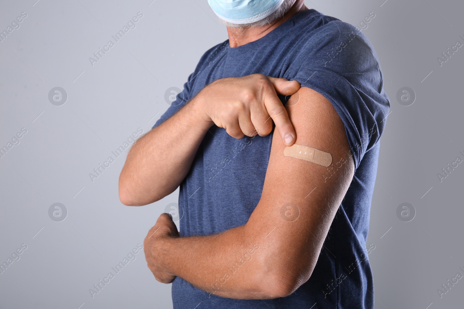 Photo of Senior man in protective mask pointing at arm with bandage after vaccination on grey background, closeup