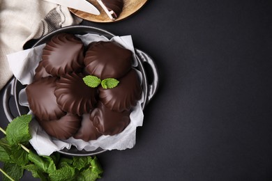 Photo of Delicious chocolate covered marshmallows with mint on black table, flat lay. Space for text