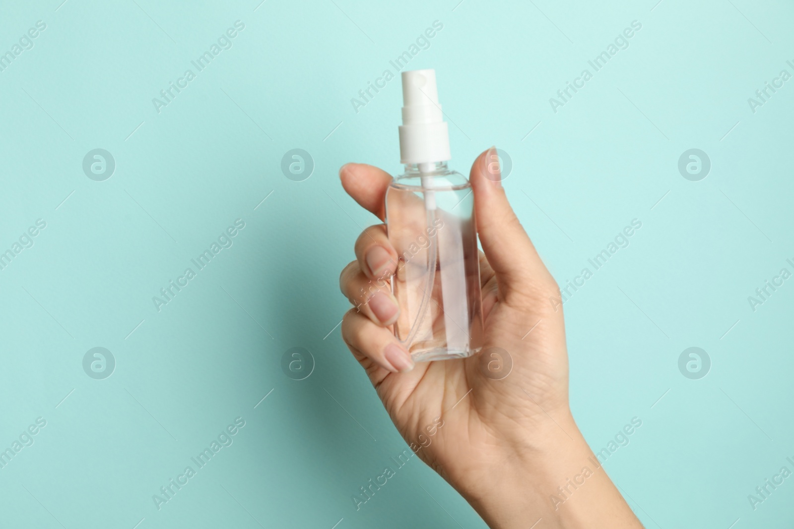 Photo of Woman holding antiseptic spray on light blue background, closeup