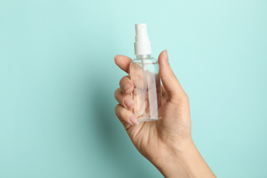 Woman holding antiseptic spray on light blue background, closeup