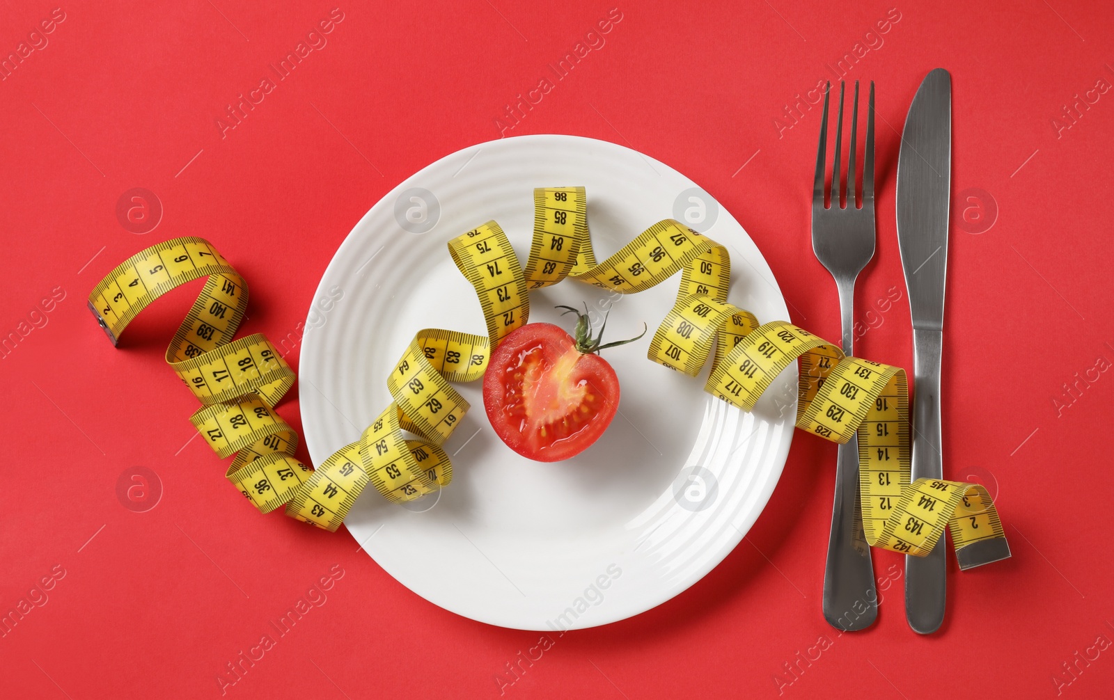 Photo of Plate with half of tomato, cutlery and measuring tape on red background, flat lay. Diet concept