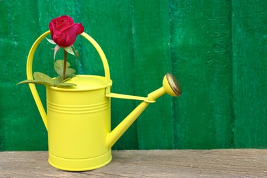 Photo of Yellow watering can with beautiful rose on wooden table. Space for text