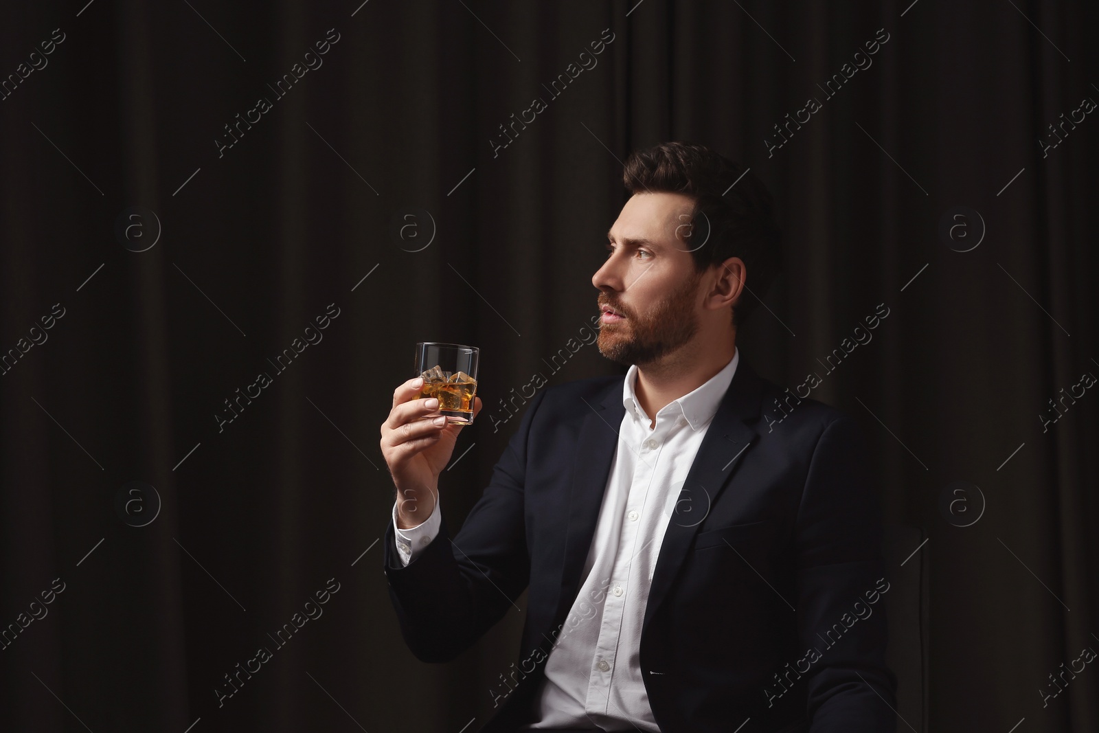 Photo of Handsome man in suit holding glass of whiskey on black background