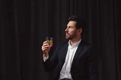 Handsome man in suit holding glass of whiskey on black background