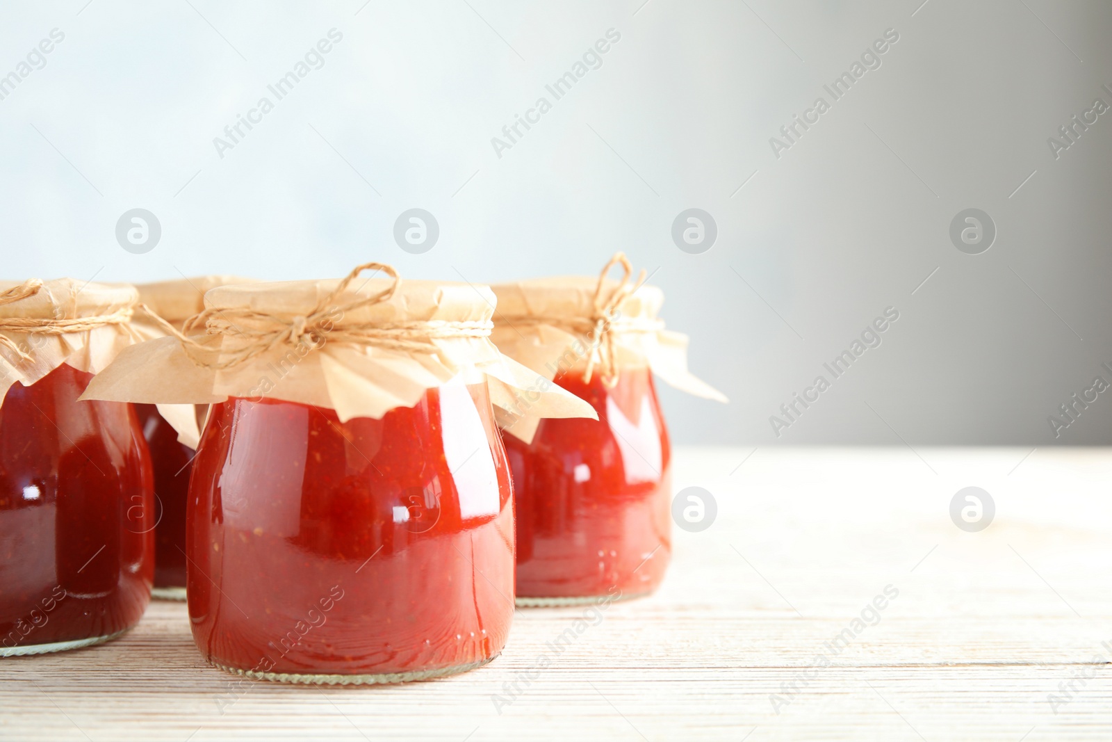 Photo of Jars of tomato sauce on wooden table against grey background, space for text