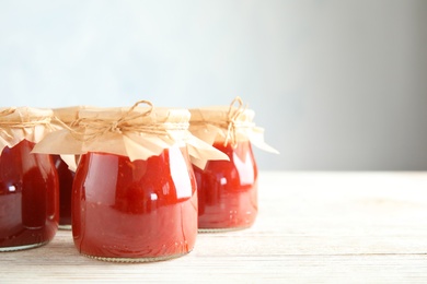 Photo of Jars of tomato sauce on wooden table against grey background, space for text