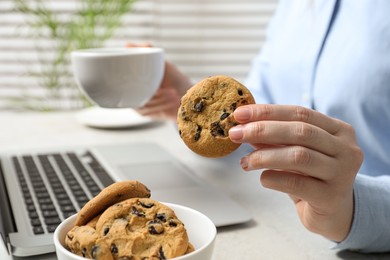 Photo of Office worker with chocolate chip cookie and cup of drink at light gray table indoors, closeup