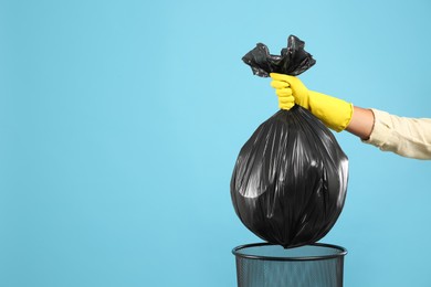 Photo of Woman taking garbage bag out of bin on light blue background, closeup. Space for text