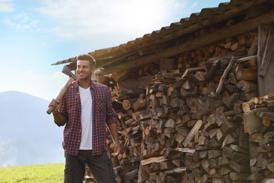 Photo of Happy man with ax near wood pile outdoors