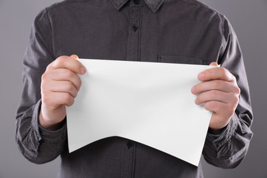 Man holding sheet of paper on grey background, closeup. Mockup for design