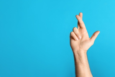 Photo of Man with crossed fingers and space for text on light blue background, closeup. Superstition concept