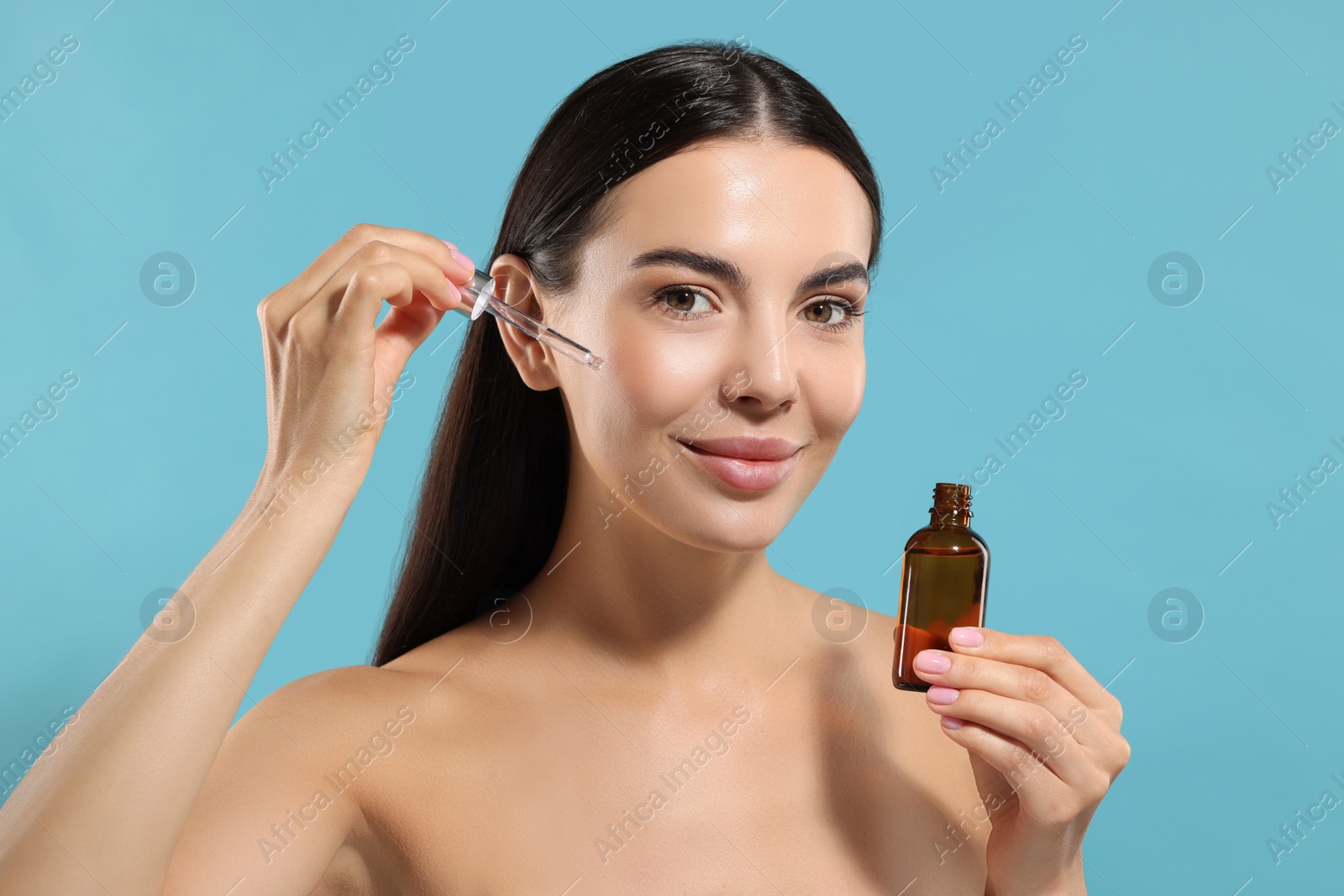 Photo of Beautiful young woman applying serum onto her face on light blue background