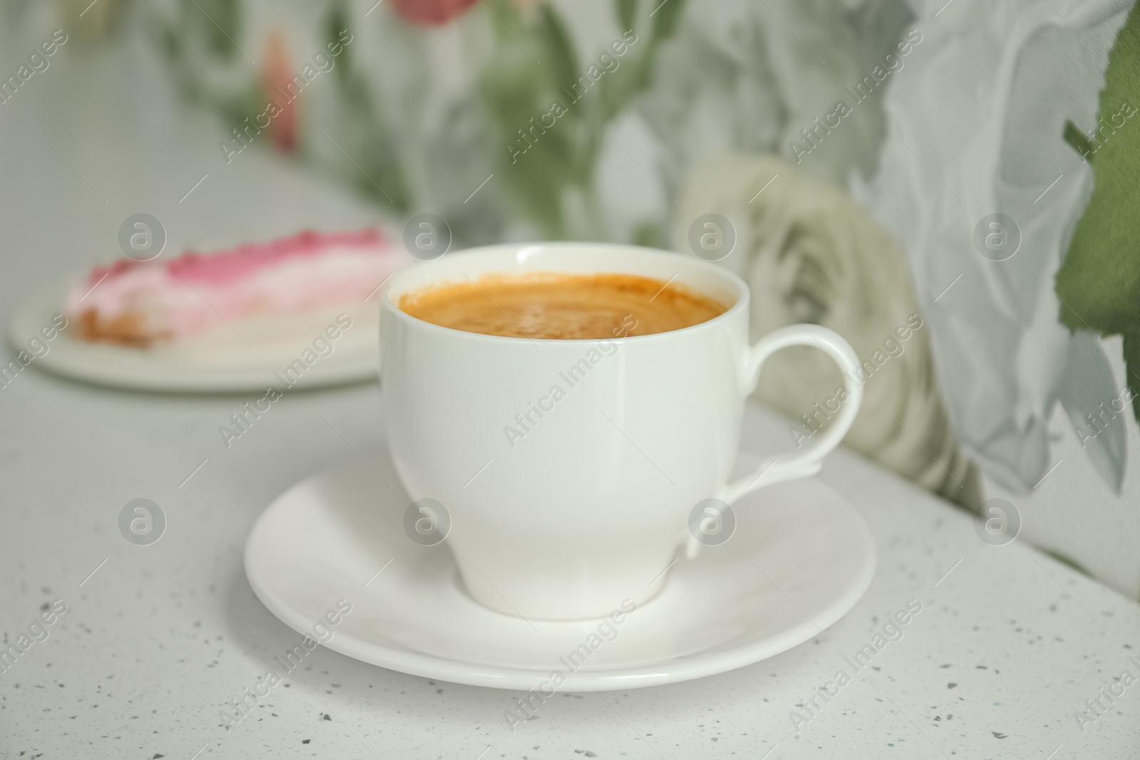 Photo of Cup of delicious aromatic coffee and eclair on white table indoors, closeup