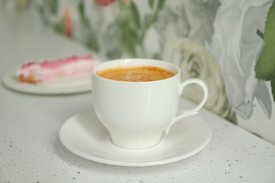 Cup of delicious aromatic coffee and eclair on white table indoors, closeup