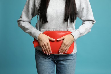 Photo of Woman using hot water bottle to relieve menstrual pain on light blue background, closeup