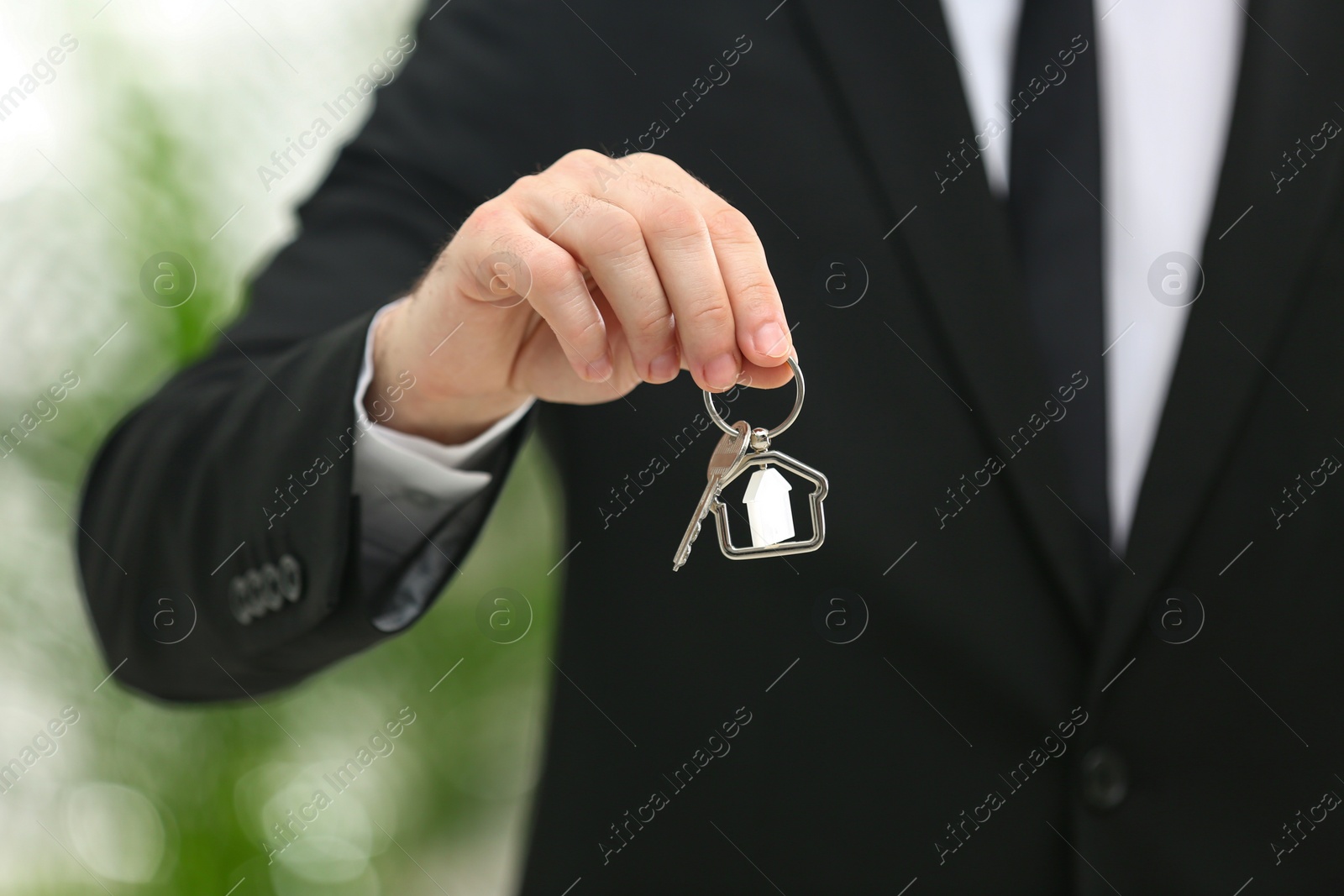 Photo of Real estate agent holding house key with trinket on blurred background, closeup