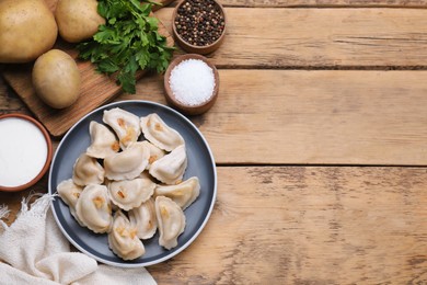 Delicious dumplings (varenyky) with potatoes and onion on wooden table, flat lay. Space for text