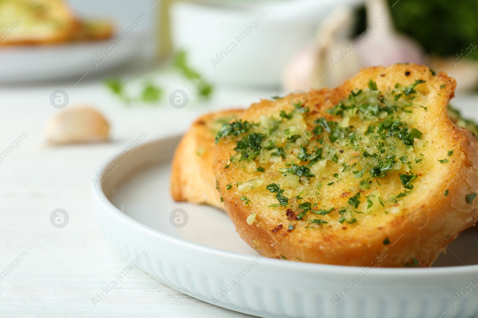 Photo of Slices of toasted bread with garlic and herbs on white wooden table, closeup