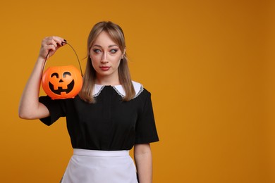 Photo of Woman in scary maid costume with pumpkin bucket on orange background, space for text. Halloween celebration