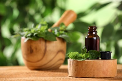 Photo of Glass bottle of nettle oil and leaves on wooden table against blurred background, space for text