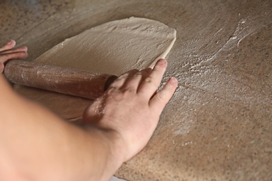 Photo of Man preparing dough for pizza at table, closeup. Oven recipe