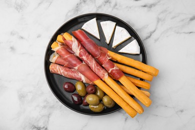Photo of Plate of delicious grissini sticks with prosciutto, cheese and olives on white marble table, top view