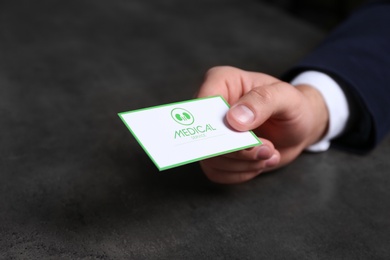 Man holding medical business card on dark background, closeup. Nephrology service