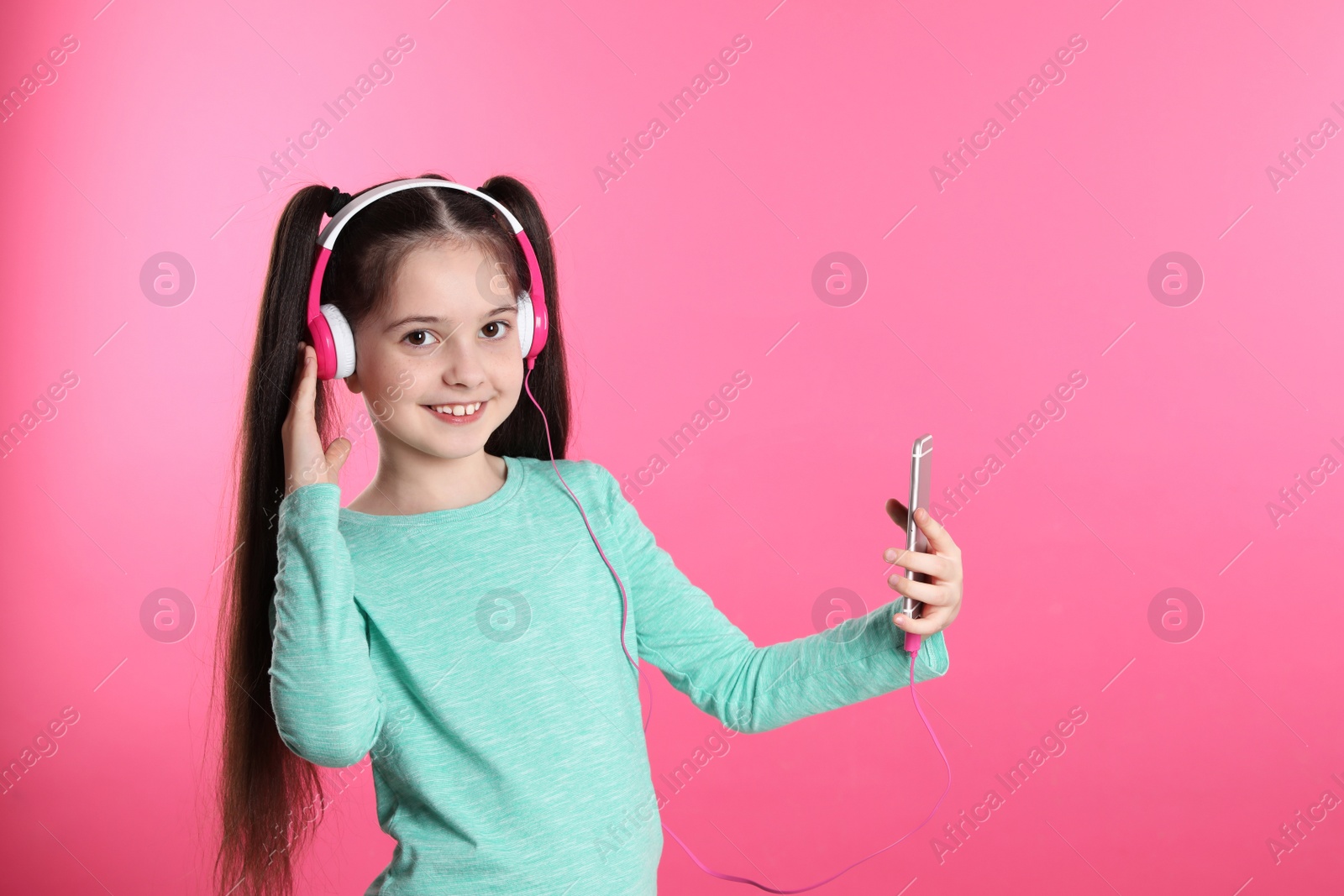 Photo of Cute girl with mobile phone enjoying music in headphones on color background. Space for text