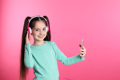 Cute girl with mobile phone enjoying music in headphones on color background. Space for text