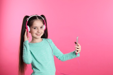 Photo of Cute girl with mobile phone enjoying music in headphones on color background. Space for text