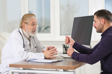 Senior doctor consulting patient at wooden table in clinic