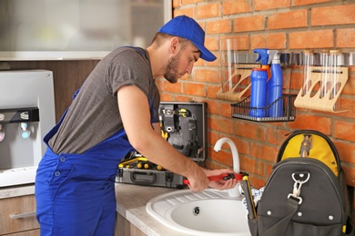 Professional plumber in uniform fixing kitchen sink